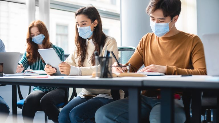 Diverse students in masks sitting at desk in classroom