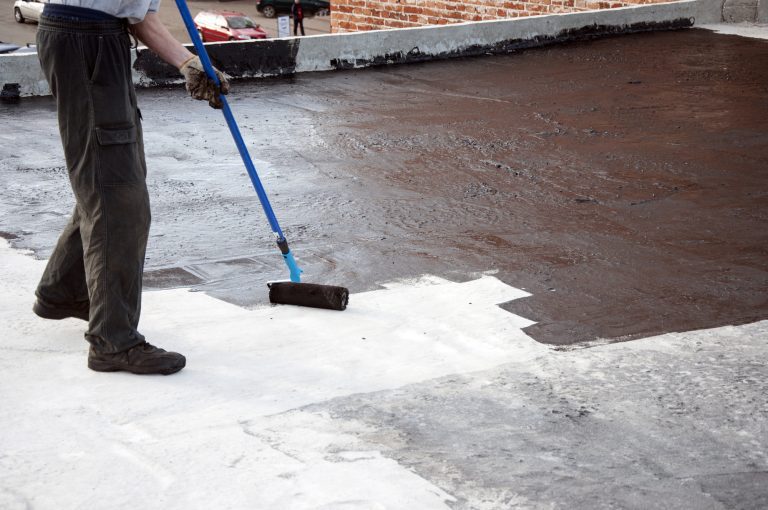 Roofer worker painting  bitumen praimer at concrete surface by t