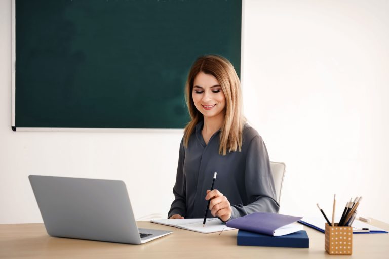 Young female teacher working at table in classroom